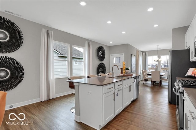 kitchen with a sink, white cabinets, appliances with stainless steel finishes, dark wood-style floors, and an island with sink