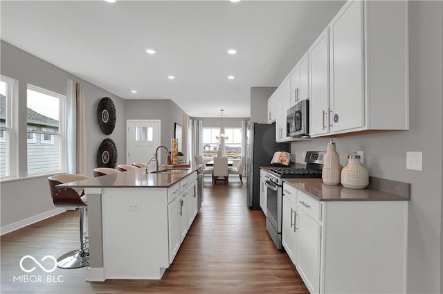 kitchen featuring stainless steel appliances, a sink, dark wood-style floors, an island with sink, and dark countertops