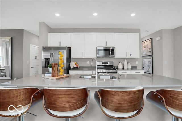 kitchen featuring recessed lighting, appliances with stainless steel finishes, white cabinets, a sink, and a large island with sink