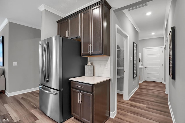 kitchen with light countertops, decorative backsplash, ornamental molding, freestanding refrigerator, and dark brown cabinets