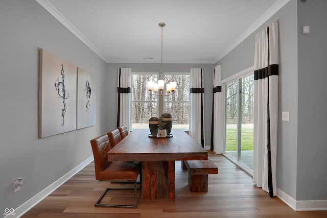 dining space featuring light wood-style floors, crown molding, baseboards, and a notable chandelier