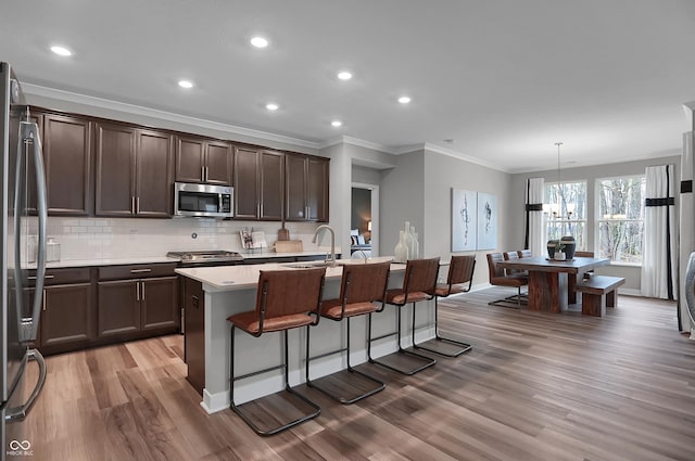 kitchen with dark brown cabinetry, wood finished floors, a sink, a kitchen breakfast bar, and appliances with stainless steel finishes