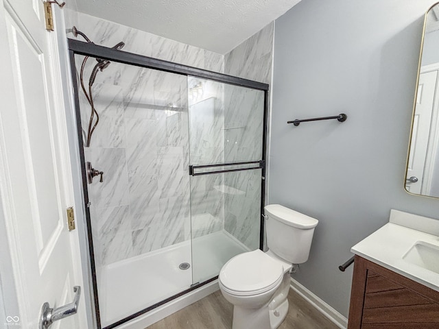 bathroom with toilet, vanity, a shower with shower door, hardwood / wood-style flooring, and a textured ceiling