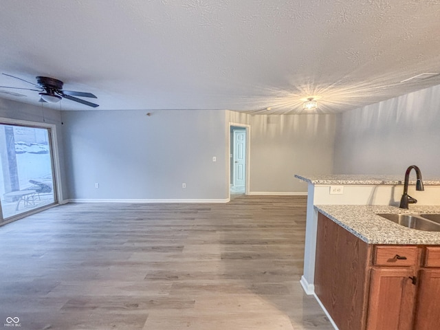 kitchen with sink, a textured ceiling, light stone counters, ceiling fan, and light hardwood / wood-style floors