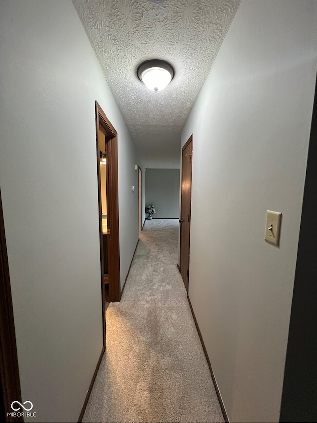 corridor with light carpet and a textured ceiling