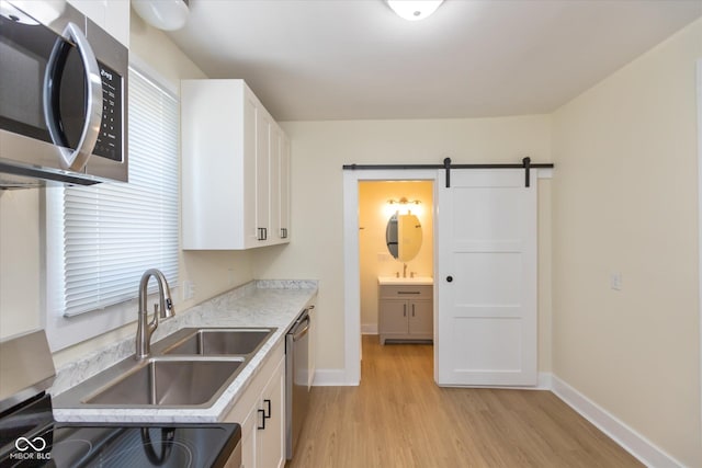 kitchen with light hardwood / wood-style flooring, stainless steel appliances, a barn door, and white cabinets