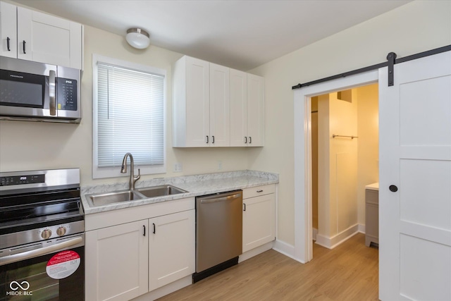 kitchen featuring sink, light hardwood / wood-style flooring, white cabinetry, stainless steel appliances, and a barn door