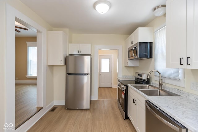 kitchen featuring light stone counters, light wood-type flooring, ceiling fan, stainless steel appliances, and white cabinets