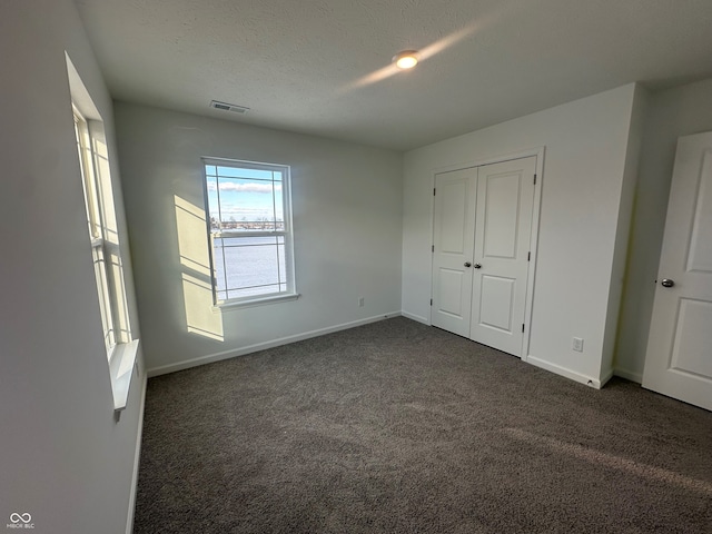 unfurnished bedroom with a textured ceiling, a closet, and dark carpet