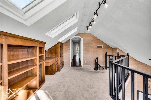 additional living space with a textured ceiling, wooden walls, vaulted ceiling with skylight, built in shelves, and carpet