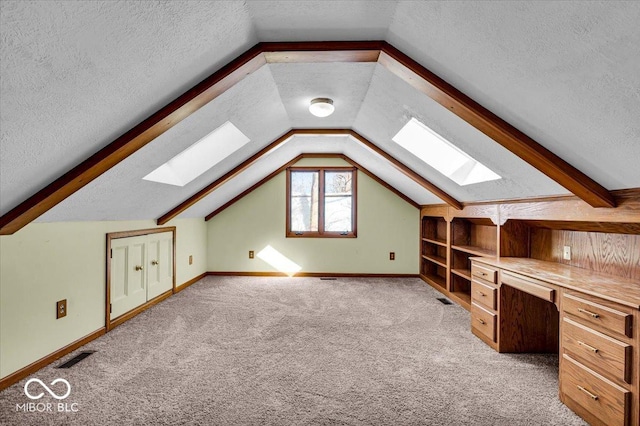 additional living space featuring built in desk, a textured ceiling, vaulted ceiling with skylight, and light colored carpet