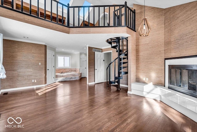 unfurnished living room with crown molding, a towering ceiling, a fireplace, and hardwood / wood-style flooring