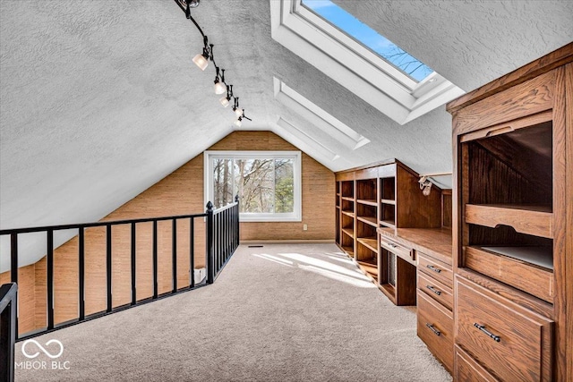 additional living space featuring a textured ceiling, light colored carpet, lofted ceiling with skylight, and wood walls