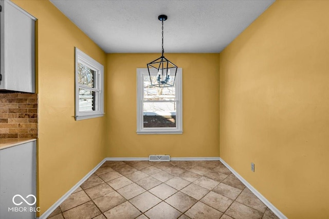 unfurnished dining area with light tile patterned flooring, a textured ceiling, and an inviting chandelier