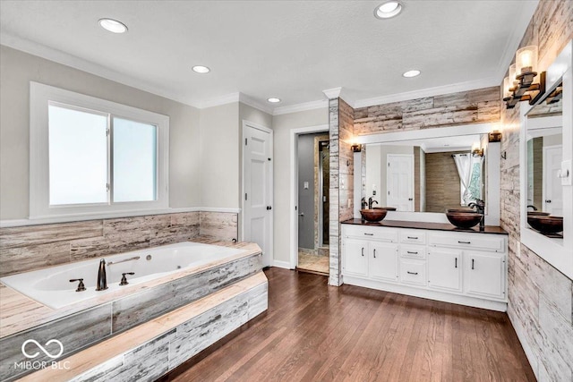 bathroom featuring hardwood / wood-style flooring, ornamental molding, tiled tub, and vanity