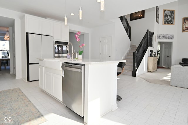 kitchen featuring decorative light fixtures, a kitchen bar, a kitchen island with sink, stainless steel appliances, and white cabinets