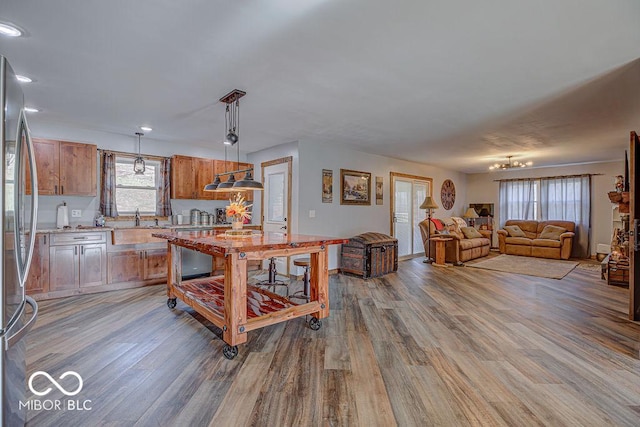 kitchen featuring stainless steel fridge, sink, hanging light fixtures, and light hardwood / wood-style floors