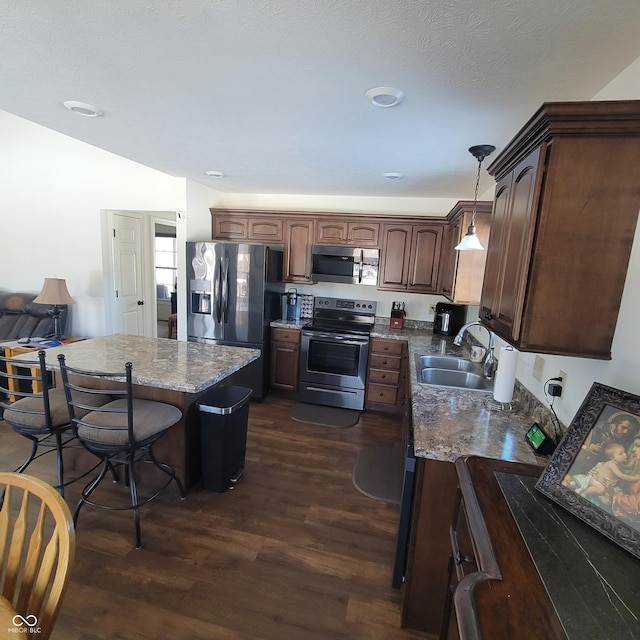 kitchen with stainless steel appliances, dark wood-type flooring, sink, dark stone countertops, and hanging light fixtures