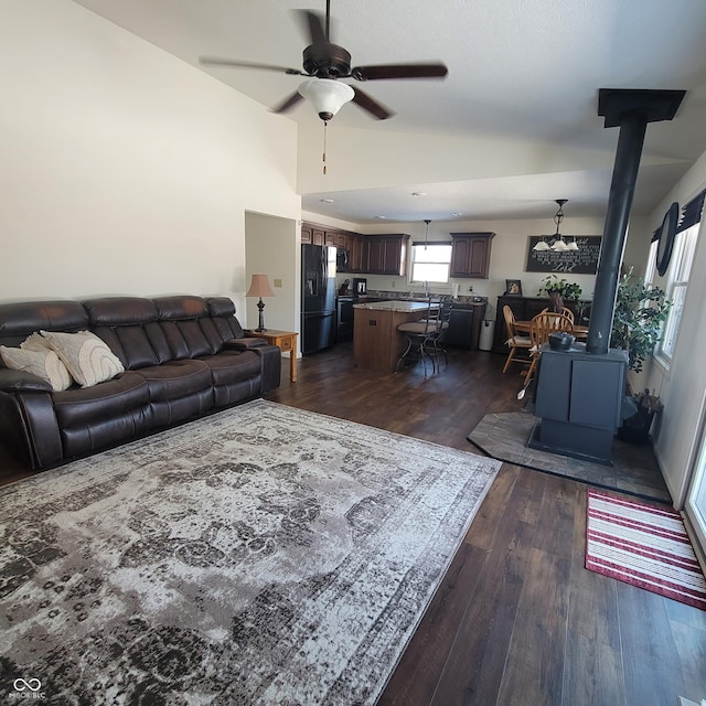 living room with a wood stove, ceiling fan, dark wood-type flooring, and vaulted ceiling