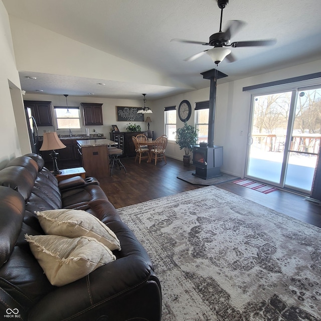 living room featuring a wood stove, ceiling fan, sink, dark wood-type flooring, and lofted ceiling