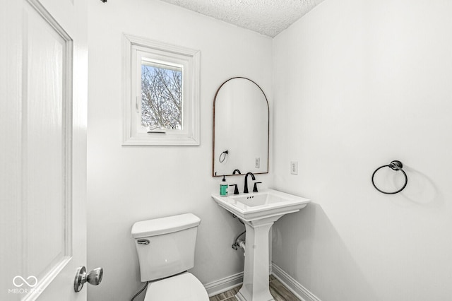 half bath with toilet, baseboards, and a textured ceiling