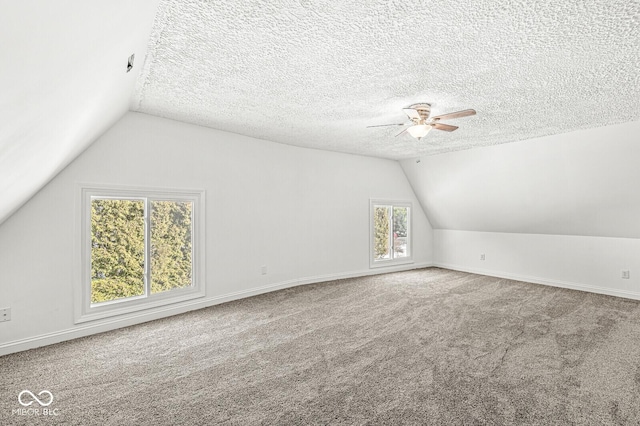 additional living space featuring a textured ceiling, carpet, baseboards, ceiling fan, and vaulted ceiling