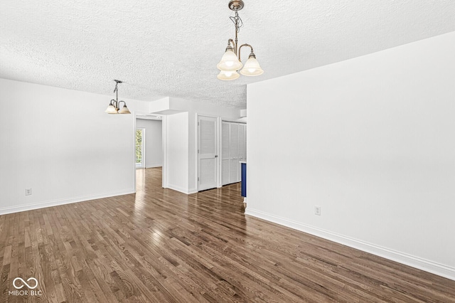 unfurnished room with a notable chandelier, wood finished floors, baseboards, and a textured ceiling