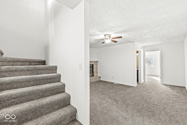 stairway featuring a ceiling fan, a textured ceiling, a fireplace, and carpet flooring