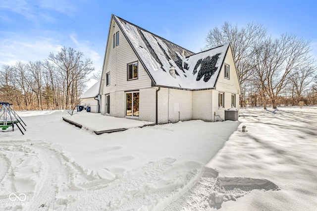 snow covered rear of property featuring central AC unit and brick siding