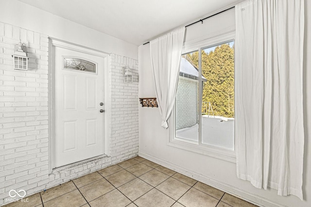 entryway with light tile patterned flooring and brick wall