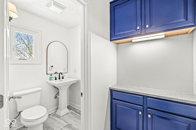 half bath featuring toilet, baseboards, visible vents, and a textured ceiling