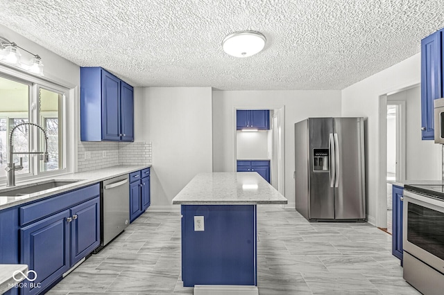 kitchen featuring blue cabinetry, a sink, stainless steel appliances, tasteful backsplash, and a center island