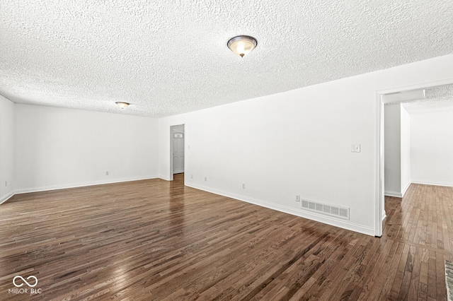 spare room featuring dark wood finished floors, visible vents, a textured ceiling, and baseboards