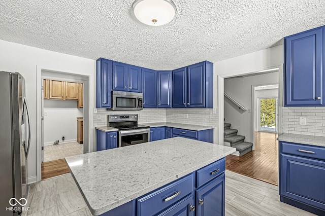 kitchen featuring tasteful backsplash, blue cabinetry, a kitchen island, light wood-type flooring, and stainless steel appliances