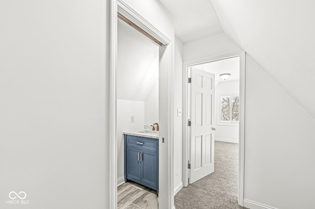 hallway featuring lofted ceiling, baseboards, and a sink