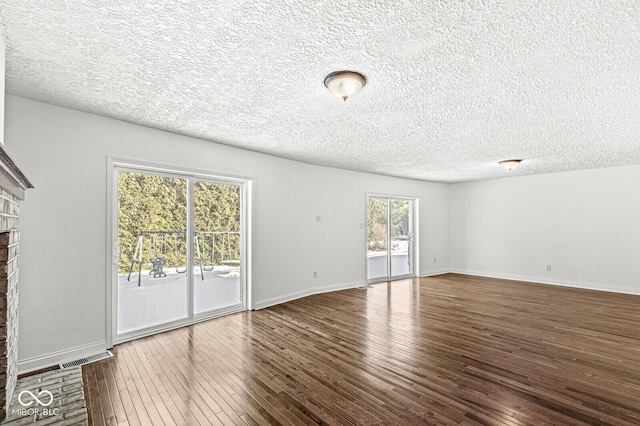 interior space featuring visible vents, a textured ceiling, wood-type flooring, baseboards, and a brick fireplace