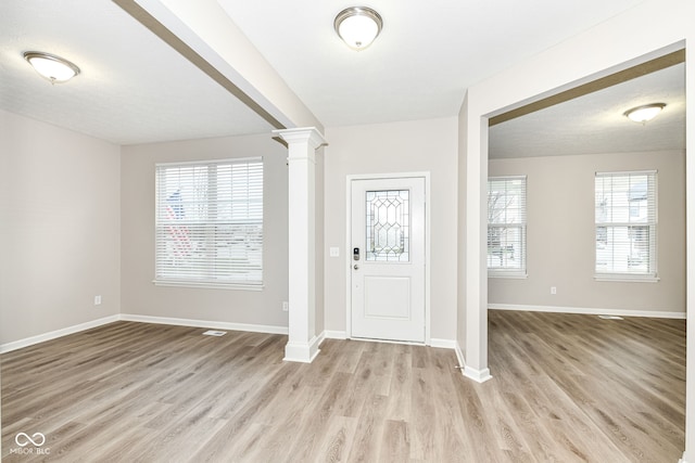 foyer entrance featuring a textured ceiling, decorative columns, and light wood-type flooring