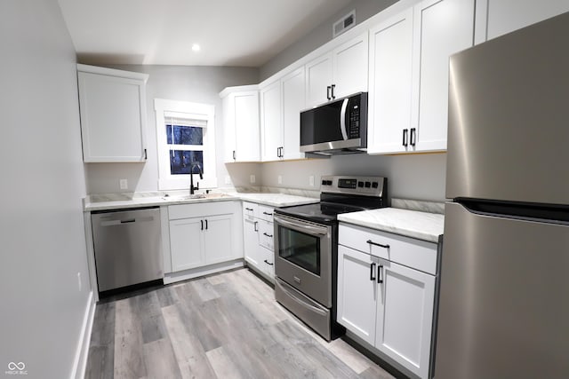 kitchen with sink, white cabinets, stainless steel appliances, light stone countertops, and light hardwood / wood-style flooring