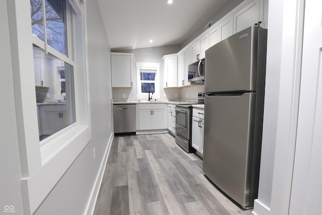 kitchen featuring vaulted ceiling, appliances with stainless steel finishes, white cabinetry, sink, and light hardwood / wood-style flooring