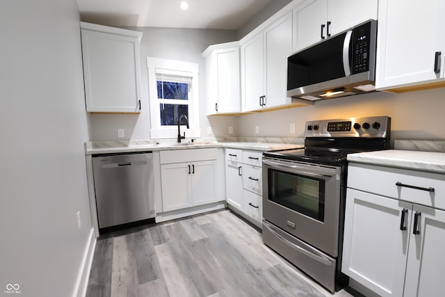 kitchen with stainless steel appliances, white cabinetry, sink, and light wood-type flooring