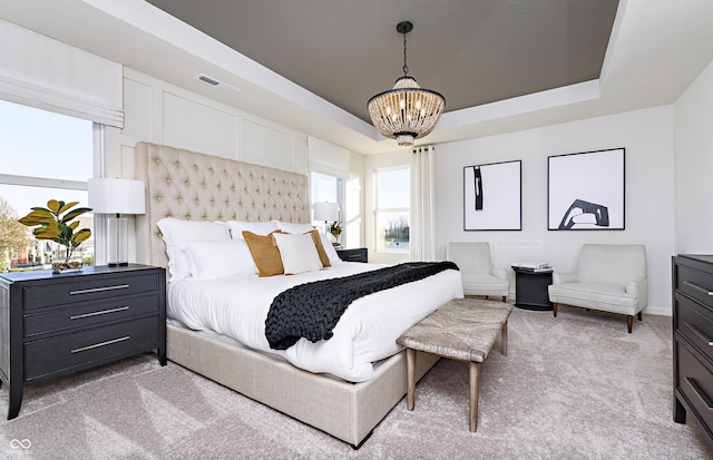 carpeted bedroom featuring an inviting chandelier and a tray ceiling