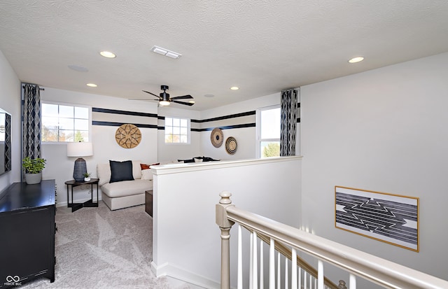 corridor featuring a textured ceiling, a healthy amount of sunlight, and light carpet