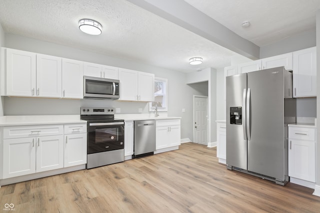 kitchen featuring stainless steel appliances, white cabinets, a textured ceiling, and light hardwood / wood-style flooring