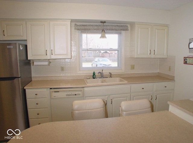 kitchen featuring backsplash, dishwasher, pendant lighting, sink, and stainless steel refrigerator