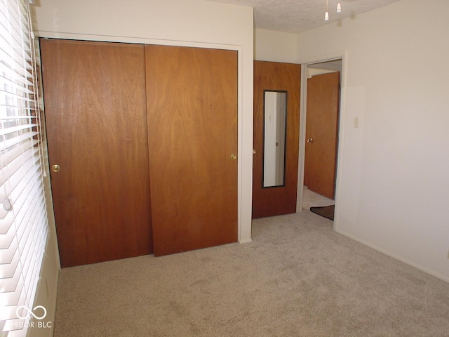 unfurnished bedroom with light colored carpet, a closet, and a textured ceiling