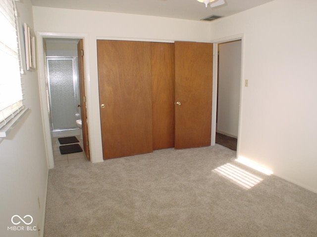 unfurnished bedroom featuring ensuite bathroom, light colored carpet, and a closet