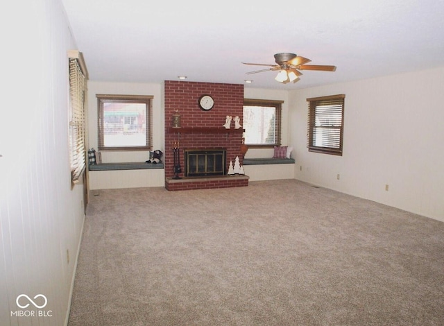 unfurnished living room featuring a brick fireplace, a wealth of natural light, carpet floors, and ceiling fan