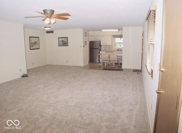 unfurnished living room featuring ceiling fan, light colored carpet, and sink