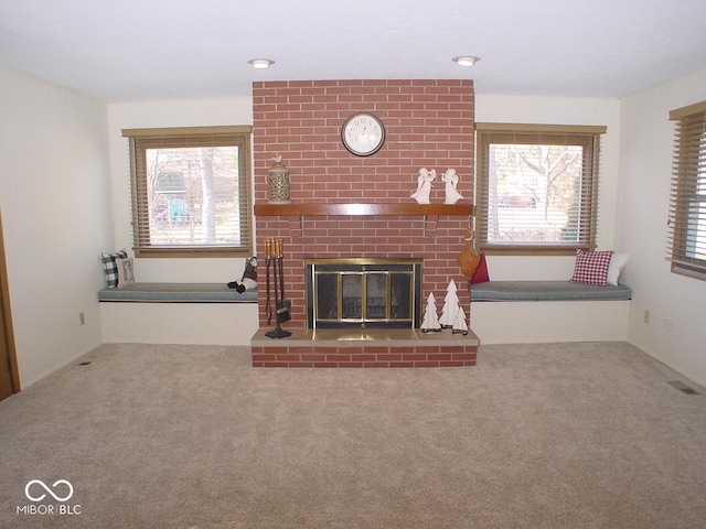 unfurnished living room with a brick fireplace, carpet, and a wealth of natural light