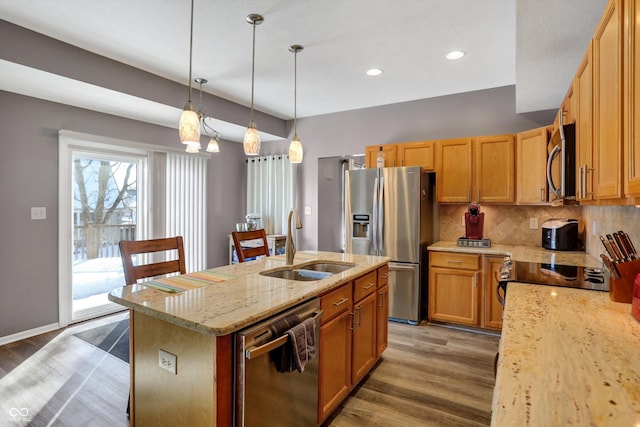 kitchen featuring sink, an island with sink, stainless steel appliances, light stone countertops, and backsplash